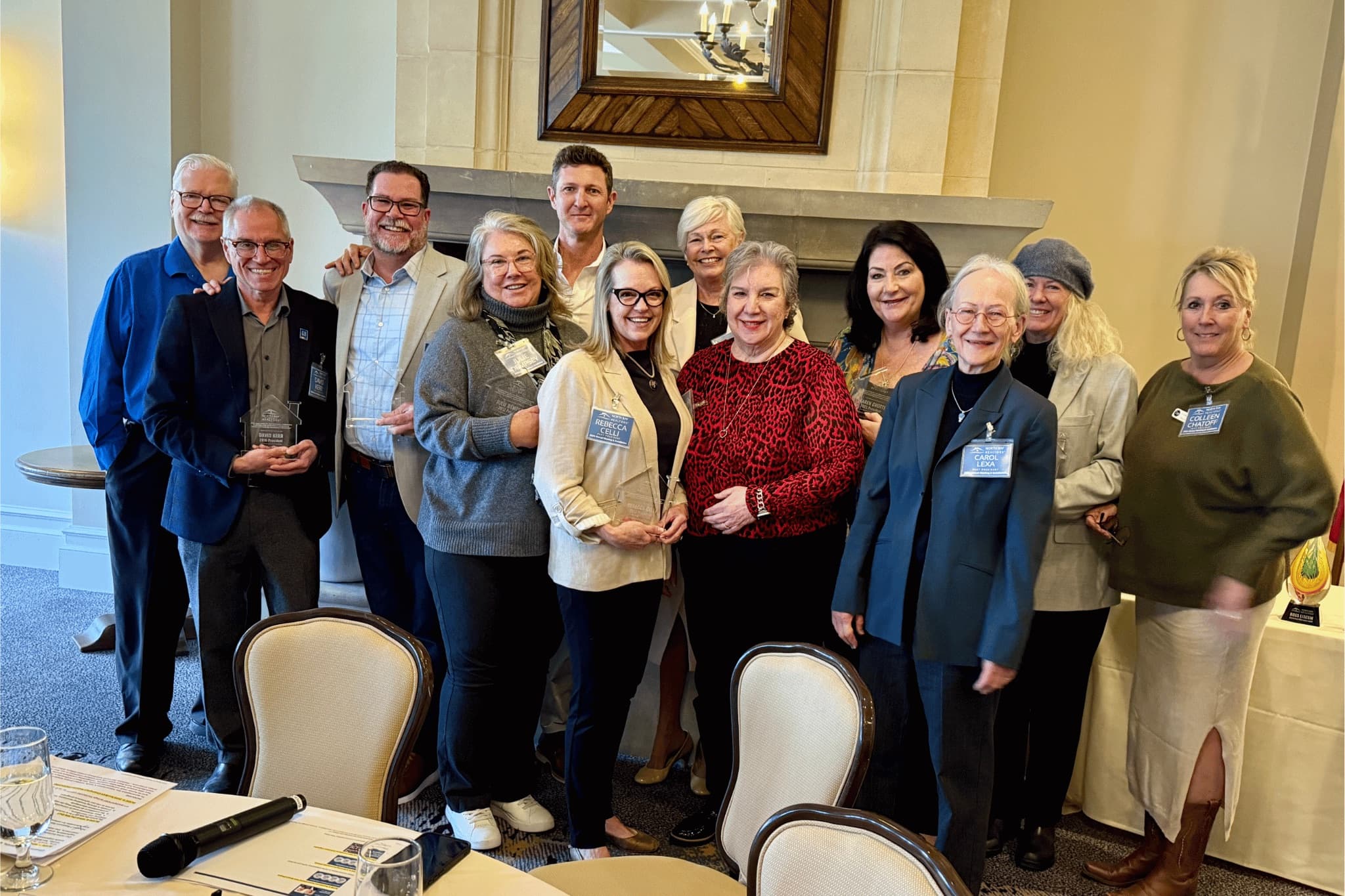 A dozen NORBAR members gathered for a photograph at an awards luncheon, several holding engraved glass house awards