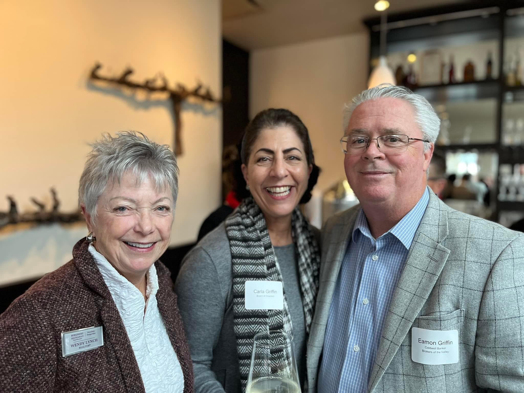 Three NORBAR members in name badges laughing together over a glass of wine at an evening mixer