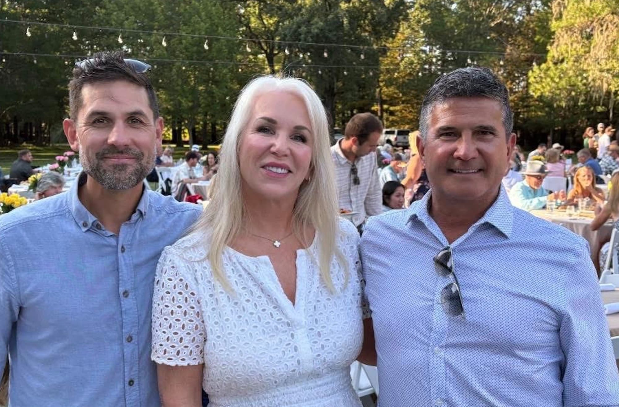 Three NORBAR members smiling together at an outdoor evening event, string lights and tables of guests behind them