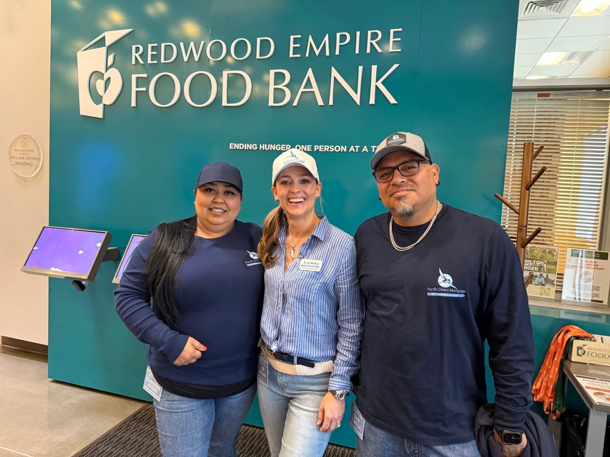 Three volunteers from an affiliate member firm smiling in front of the Redwood Empire Food Bank sign