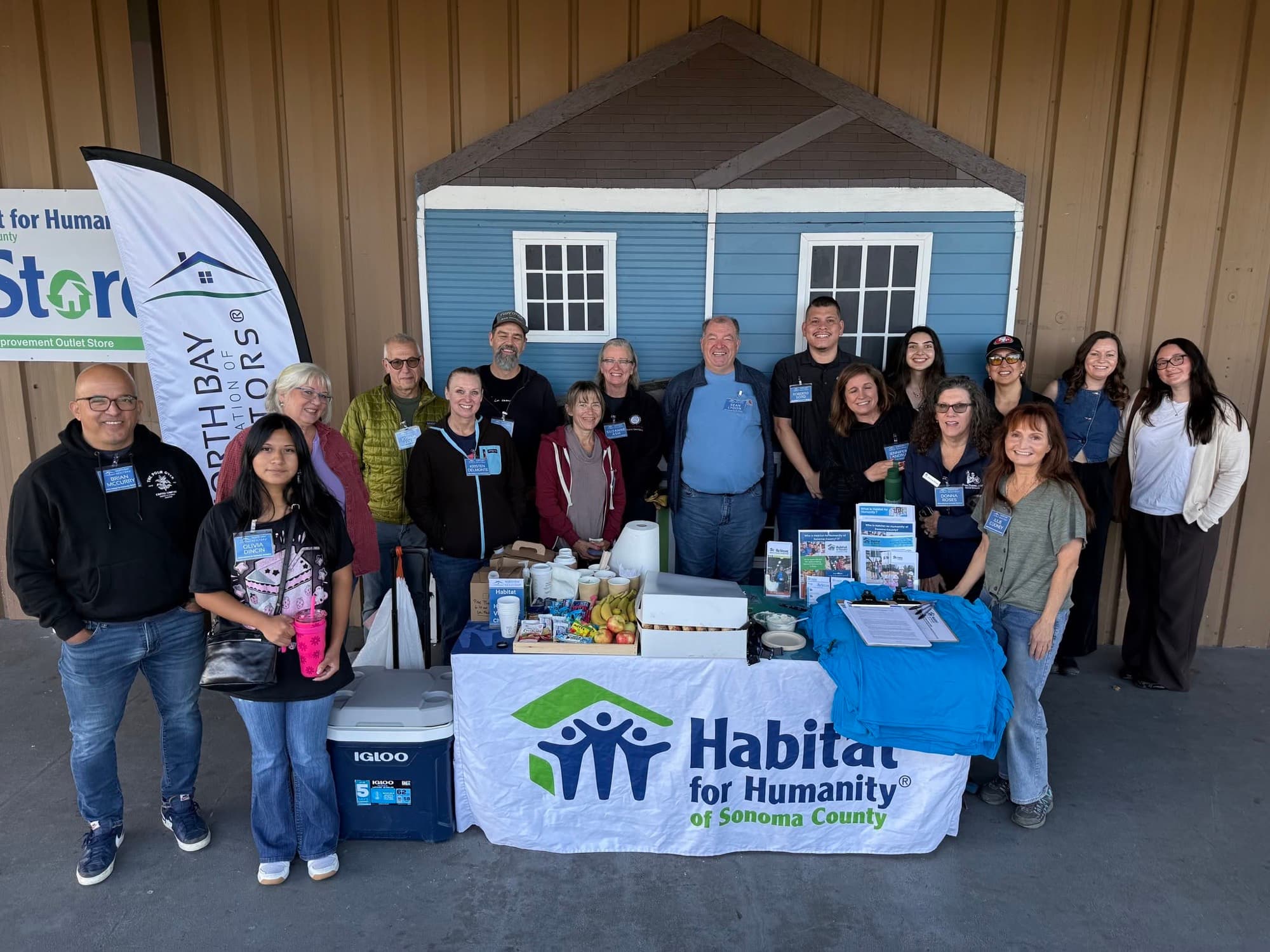 A large group of NORBAR volunteers gathered behind a Habitat for Humanity of Sonoma County table outside the ReStore