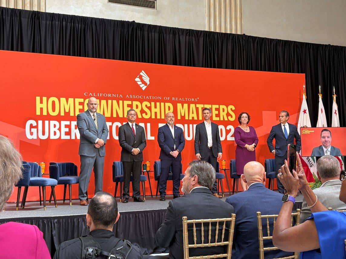 Six candidates on stage before an orange CAR Homeownership Matters Gubernatorial Forum backdrop, audience seated in front.