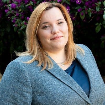 Outdoor headshot of Malissa Seiger, NORBAR's 2026 Emerging Leader, in a grey blazer in front of purple flowers.