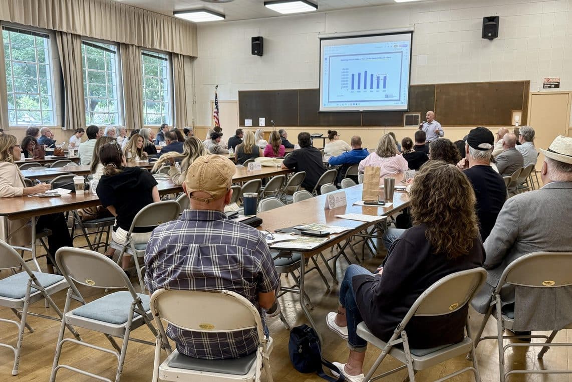 A full room of attendees watches a speaker present market data charts at the Santa Rosa Marketing Meeting mid-year review.