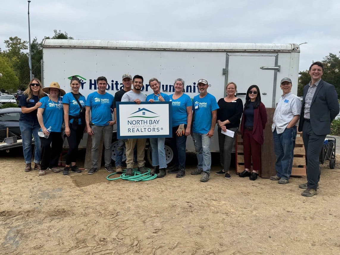 Volunteers in Habitat for Humanity shirts holding a North Bay Association of REALTORS sign in front of a Habitat trailer.
