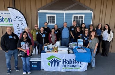 A large group of volunteers posed behind a Habitat for Humanity of Sonoma County table outside the ReStore.