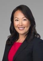 Bonnie Lau, smiling, in a black blazer over a red top against a grey background.