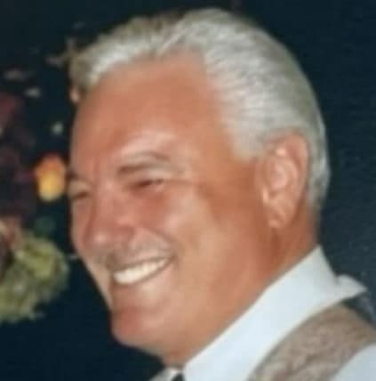 Vernon "Vern" Hansen, smiling, with grey hair, a white shirt and tie and a patterned jacket, photographed at an evening event.